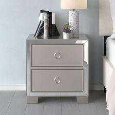 a night stand with two drawers and a lamp on it next to a white bed