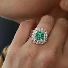 a close up of a person's hand wearing a ring with an emerald and diamond center