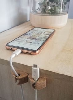 an iphone plugged in to a charger on top of a wooden table next to a potted plant