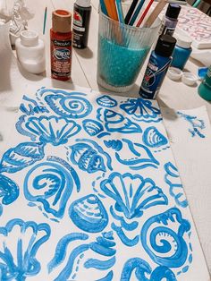 a table topped with blue and white paper covered in art supplies on top of a wooden table