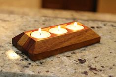 three lit candles in a wooden holder on a marble counter