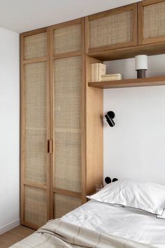 a bed with white sheets and pillows in front of a wooden shelf filled with books