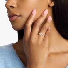 a close up of a person wearing a ring on their finger and holding her hand near her face