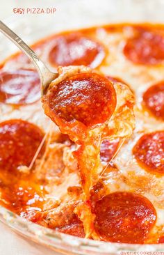 a spoon full of pepperoni pizza sauce being lifted from a casserole dish