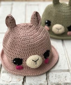 two crocheted hats with teddy bears on them sitting on a white brick floor