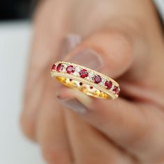 a woman's hand holding a gold ring with red and white stones