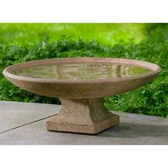 a stone bowl sitting on top of a cement table in front of some green grass