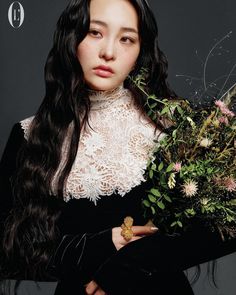 a woman with long black hair holding flowers in her hands and looking at the camera