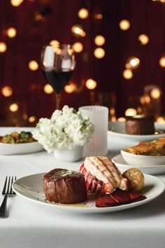 a white table topped with plates and bowls filled with food next to a glass of wine