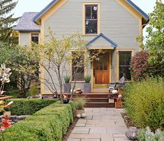 a house that is sitting in the middle of some bushes and trees, with a walkway leading to it