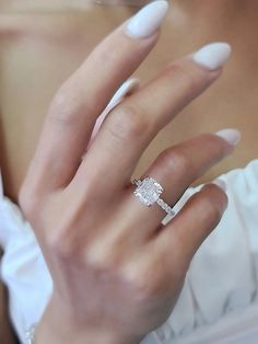 a woman's hand with a diamond ring on her left finger and white nails