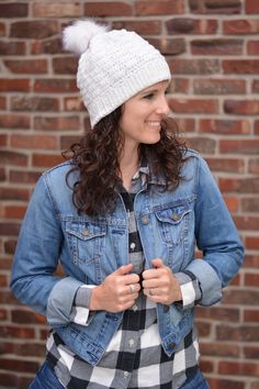 a woman standing in front of a brick wall wearing a jean jacket and a white hat