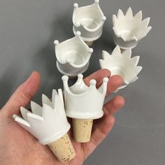 a hand is holding five white wine bottle stoppers in the shape of crownes