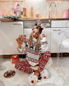 a woman sitting on the floor with christmas decorations in her hands and reindeers around her