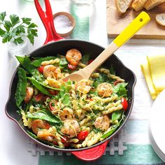 a skillet filled with vegetables and meat on top of a table next to bread