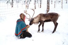 a man kneeling down next to a reindeer in the snow with it's head on his hand