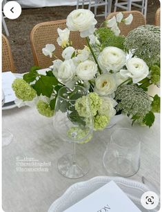 a vase filled with white flowers sitting on top of a table next to two wine glasses