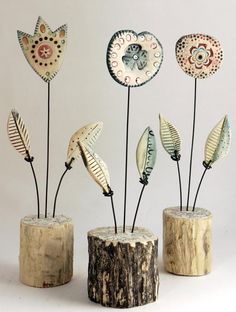 three wooden vases with metal flowers and leaves in them on top of a tree stump