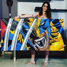 a woman standing in front of a painting holding up a large wolverine comic poster with an angry face on it