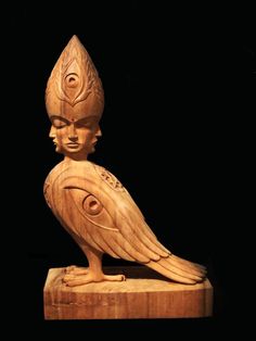 a carved wooden bird sitting on top of a wooden block in the shape of a woman's head