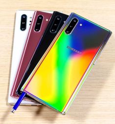 three samsung note10s are sitting next to each other on a wooden table with a pen