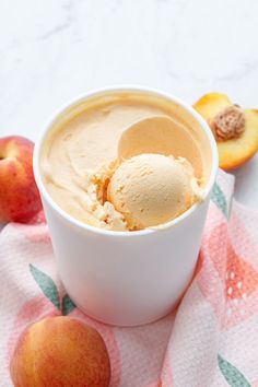 two scoops of ice cream in a white bowl next to peaches on a pink and green towel