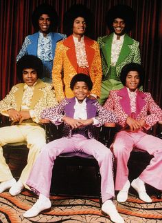 a group of men sitting on top of a couch in front of a red curtain