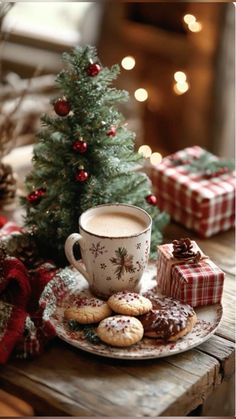 a cup of coffee and some cookies on a table next to a small christmas tree