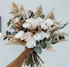 a hand holding a bouquet of white and brown flowers