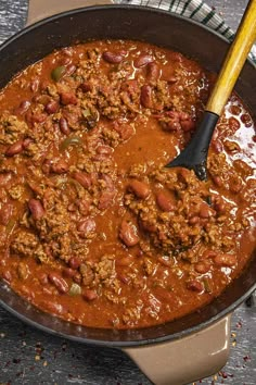 a pot filled with chili and meat on top of a table next to a wooden spoon