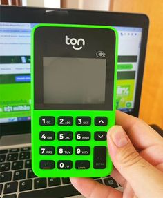 a person holding a green cell phone in front of a laptop