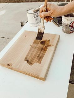 a person using a brush to paint a piece of wood on a white table outdoors