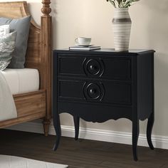 a black nightstand with two drawers next to a bed and vase on top of it