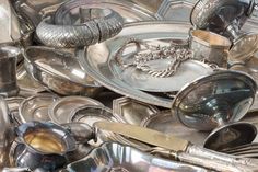 a pile of silver dishes and spoons sitting next to each other on top of a table