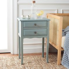 a blue table with two drawers and a glass bottle on it next to a bed