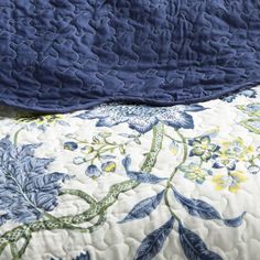 a blue and white quilted bedspread on top of a bed next to a pillow