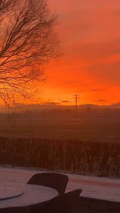 the sun is setting over a field with snow on the ground and trees in the foreground