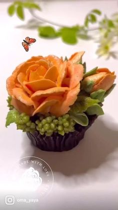 an orange rose sitting on top of a cupcake covered in green leaves and flowers