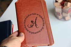 a person holding up a brown leather book with the letter a on it's cover