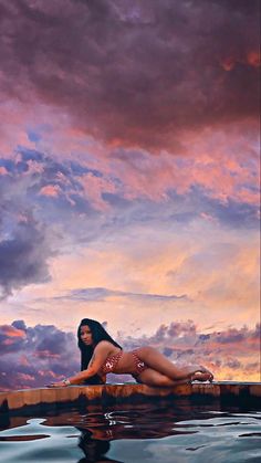 a woman in a bathing suit is sitting on the edge of a pool at sunset