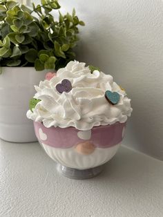 there is a cupcake with white frosting and hearts on it next to a potted plant