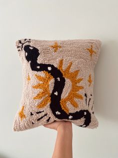 a hand holding up a decorative pillow with an image of a lizard on the front