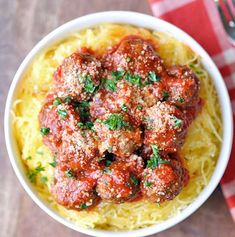 a white bowl filled with spaghetti and meatballs on top of a red checkered table cloth