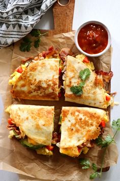 four sandwiches cut in half on top of brown paper next to a bowl of sauce