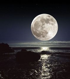 the full moon is shining brightly in the sky over the water and rocks on the beach