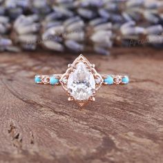 an engagement ring with a pear shaped diamond surrounded by turquoise stones on a wooden surface