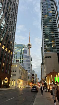 people are walking on the sidewalk in front of tall buildings and skyscrapers at dusk