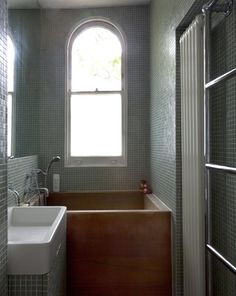 a bath tub sitting under a window next to a sink and shower head mounted faucet