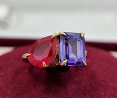 two different colored stone rings sitting on top of a red velvet cushion