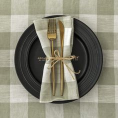 a black plate topped with a fork and knife next to a white napkin on top of a checkered table cloth